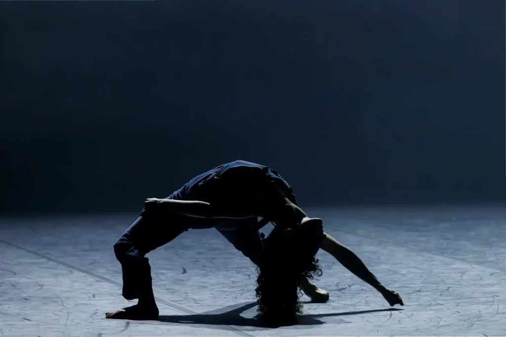 Une danseuse en pont arrière, seule dans un faisceau de lumière bleue